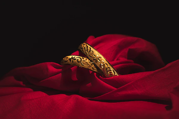 A delicate gold bangle resting on a soft beige fabric, glowing with warm light.