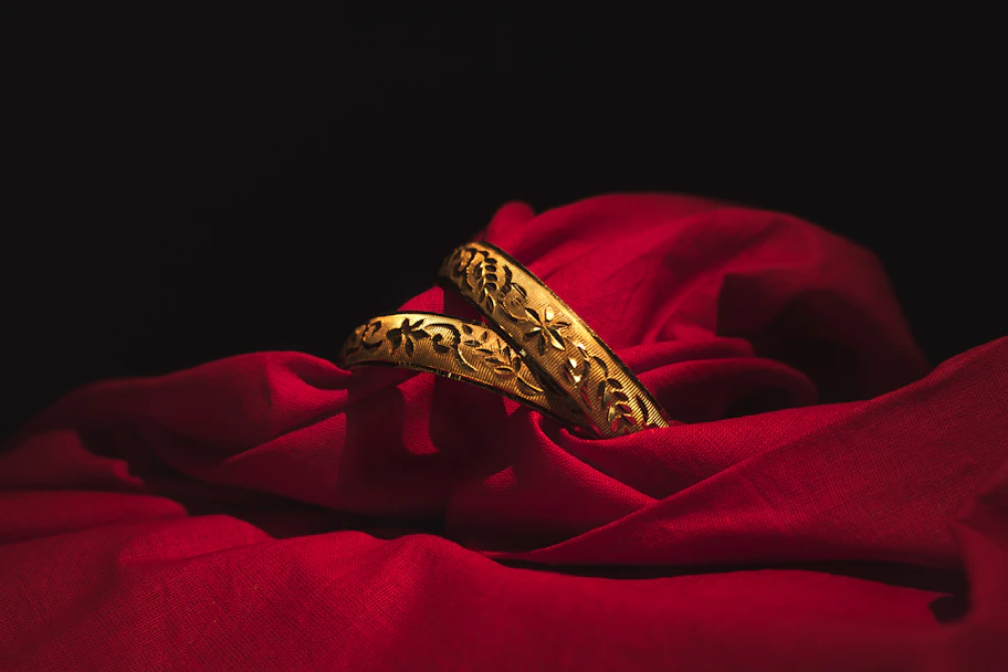 Close-up of a delicate gold bangle resting on ivory silk fabric with soft golden light highlighting its elegant curves