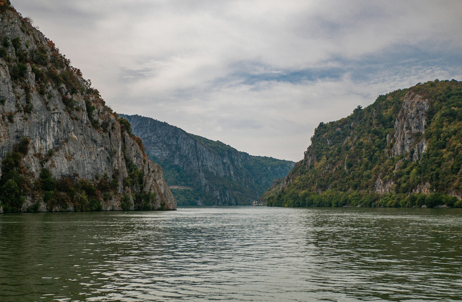 Steep forested cliffs of the Iron Gates gorge closing in on the wide, calm Danube near Orșova