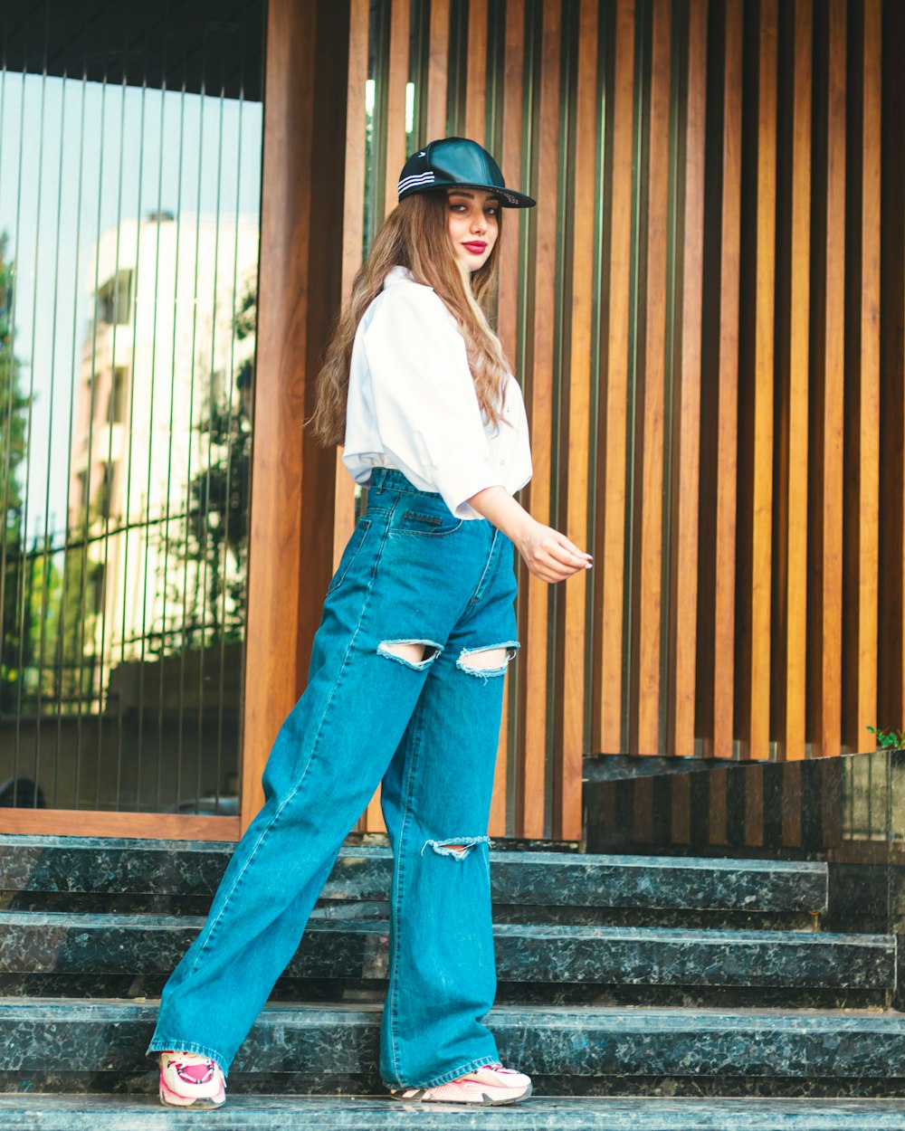a woman standing on steps wearing a hat and jeans
