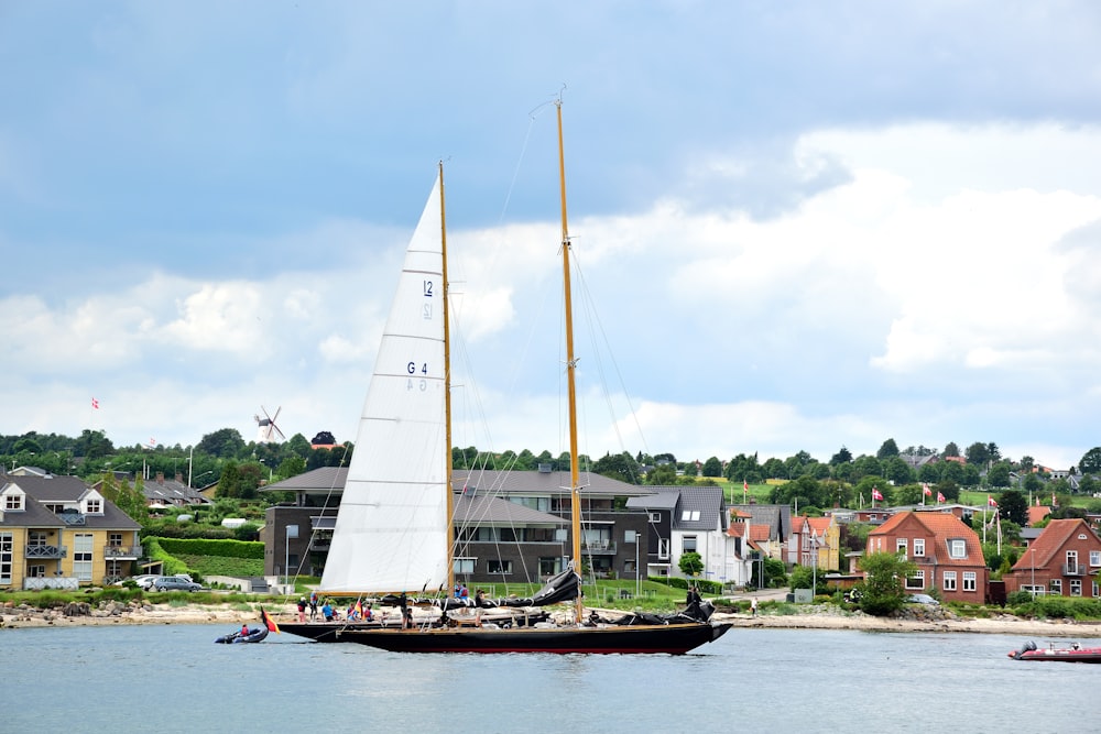 a sailboat sailing on the water in front of a row of houses
