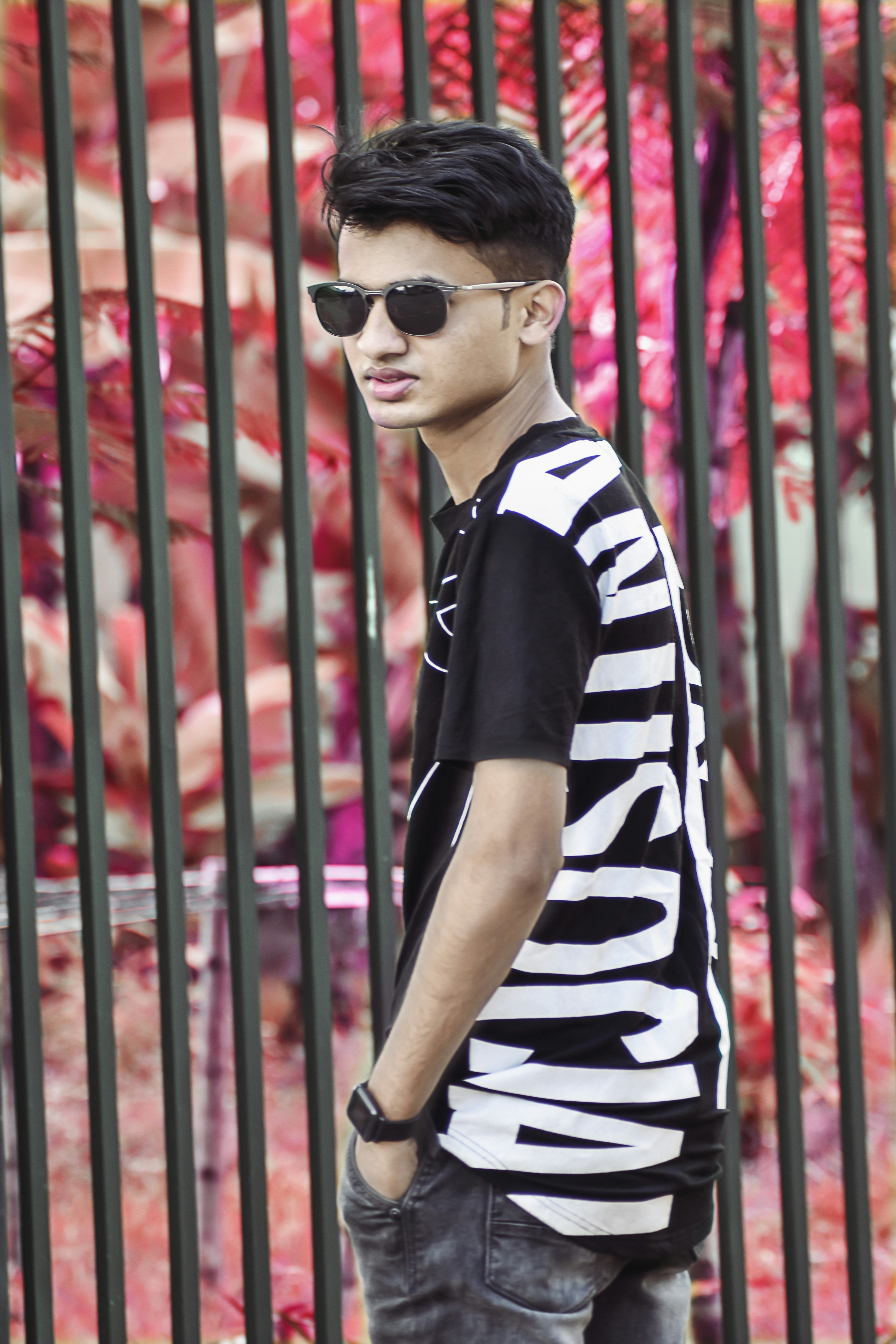 a young man wearing sunglasses standing in front of a fence