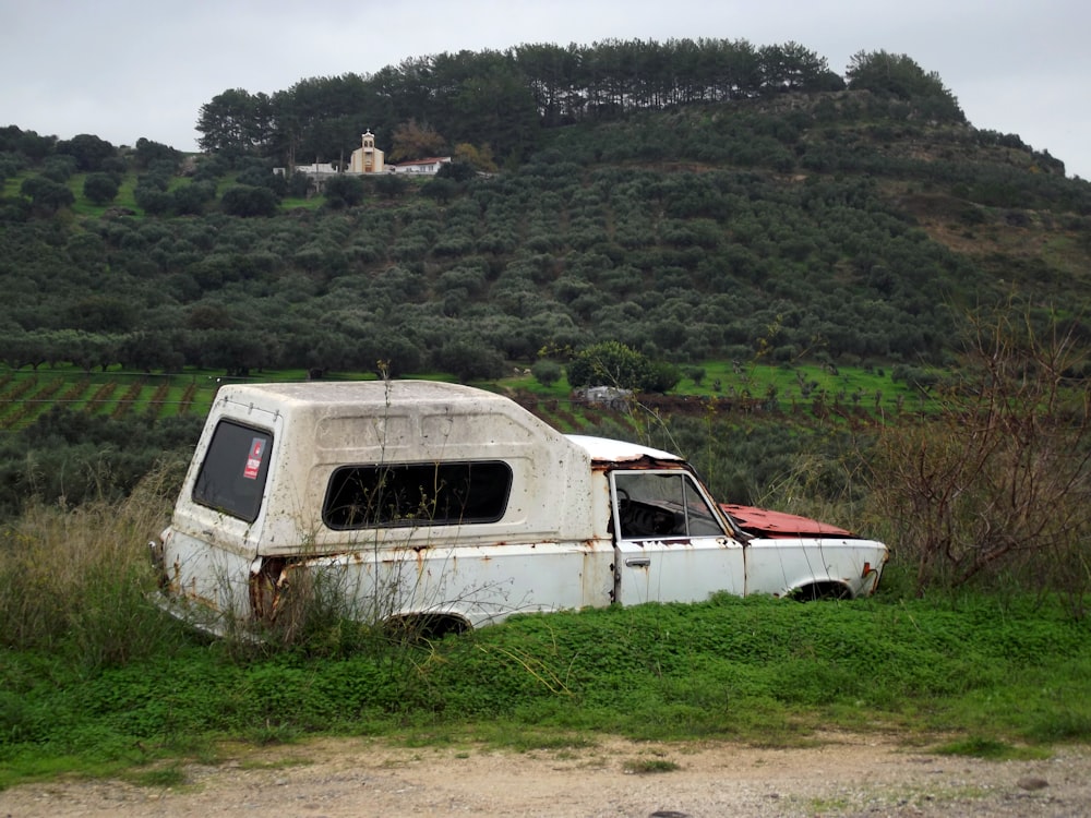 an old truck sitting in a field with a hill in the background