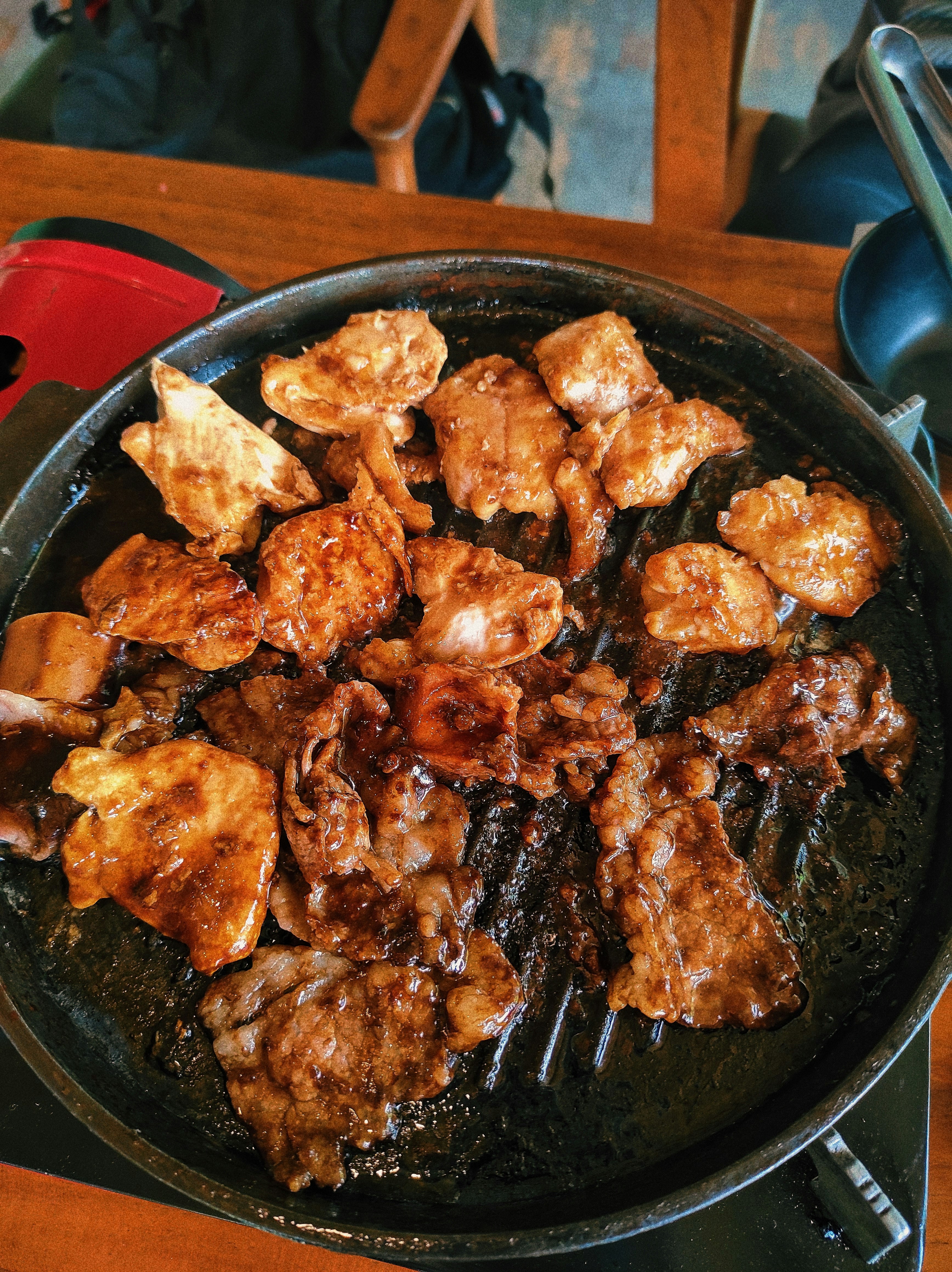 Sizzling grilled meat platter on dark wooden table, dim warm candlelight, deep amber shadows, rich dark background
