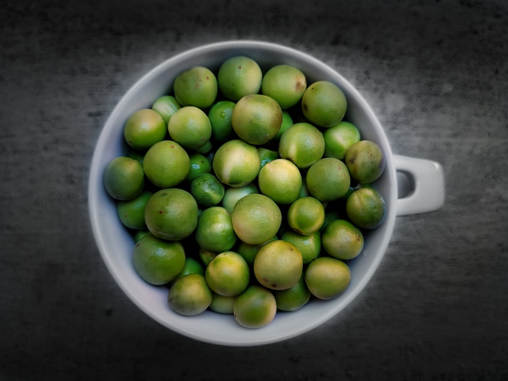 a white bowl filled with green apples on top of a table