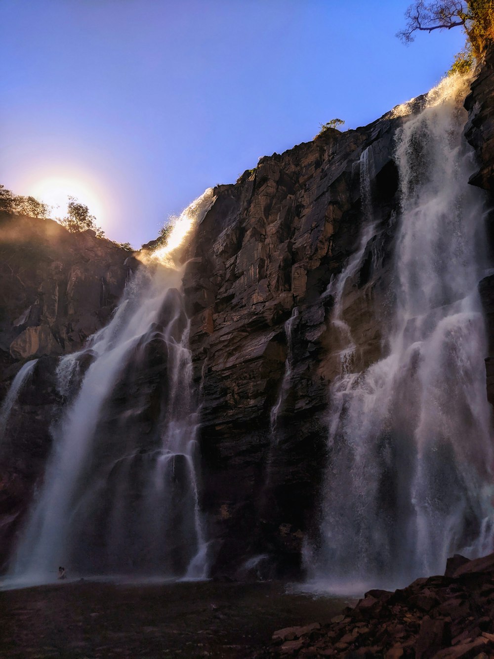 the sun is shining behind a waterfall