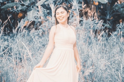 Woman smiling outdoors wearing a casual light summer dress surrounded by greenery.