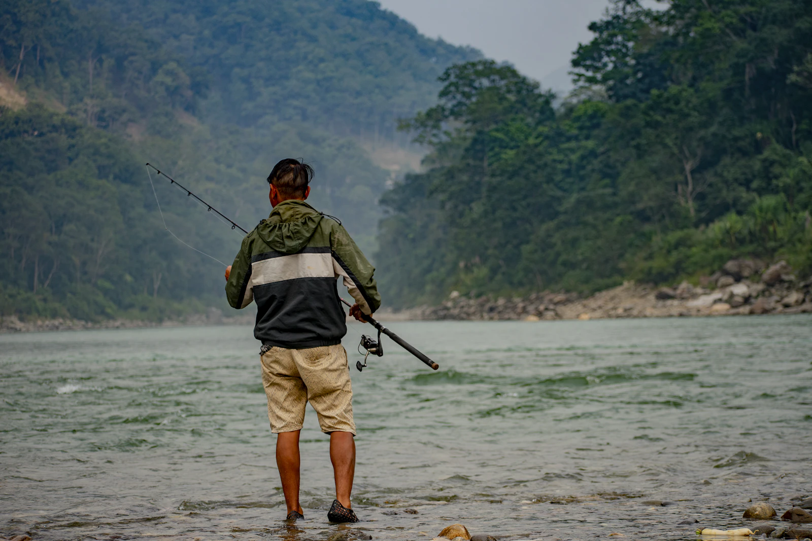An angler wading into the green water at Tribeni, where the Rangeet meets the Teesta, forested hills on both banks