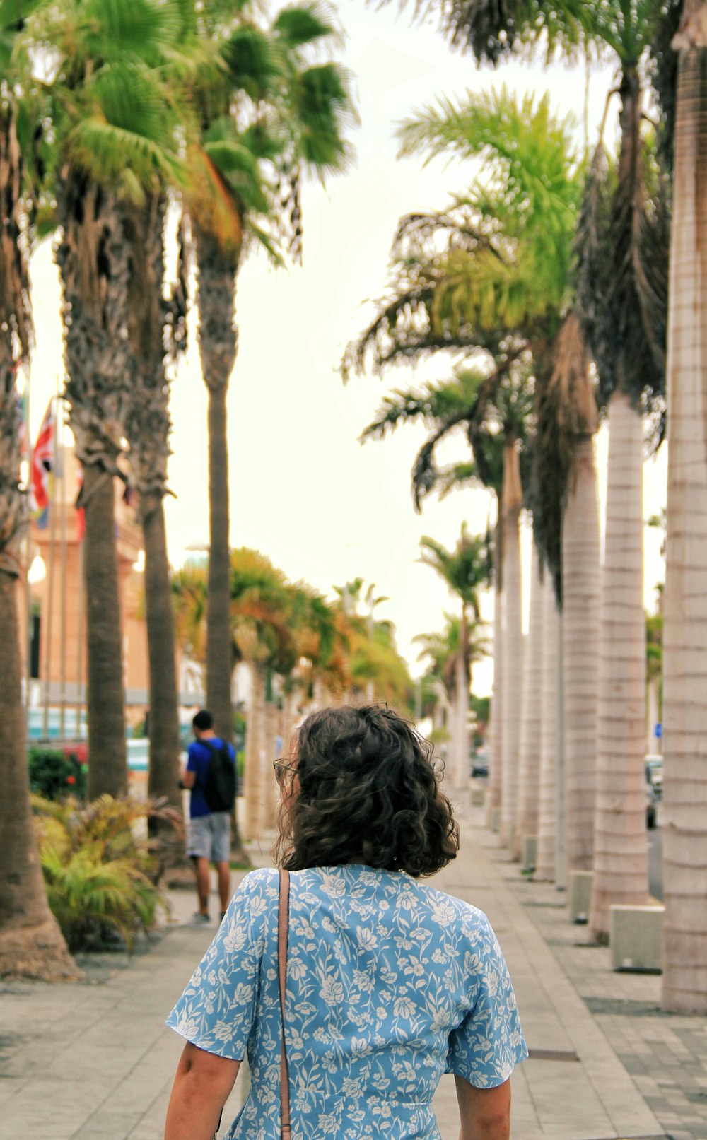 a woman walking down a sidewalk carrying a brown bag