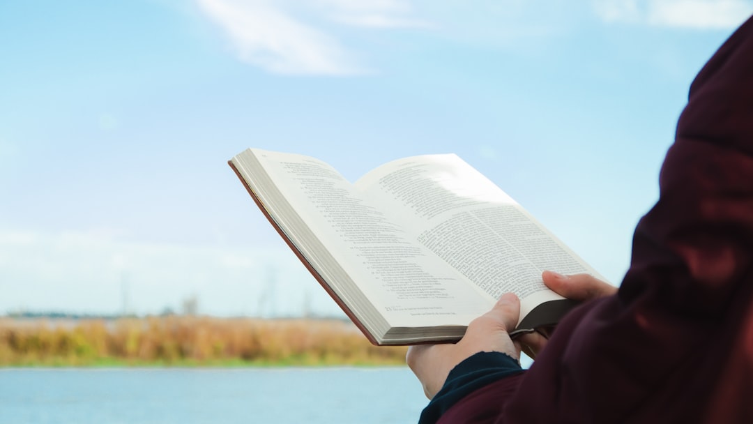 a person holding a book in their hands, Person reading Bible outdoor.