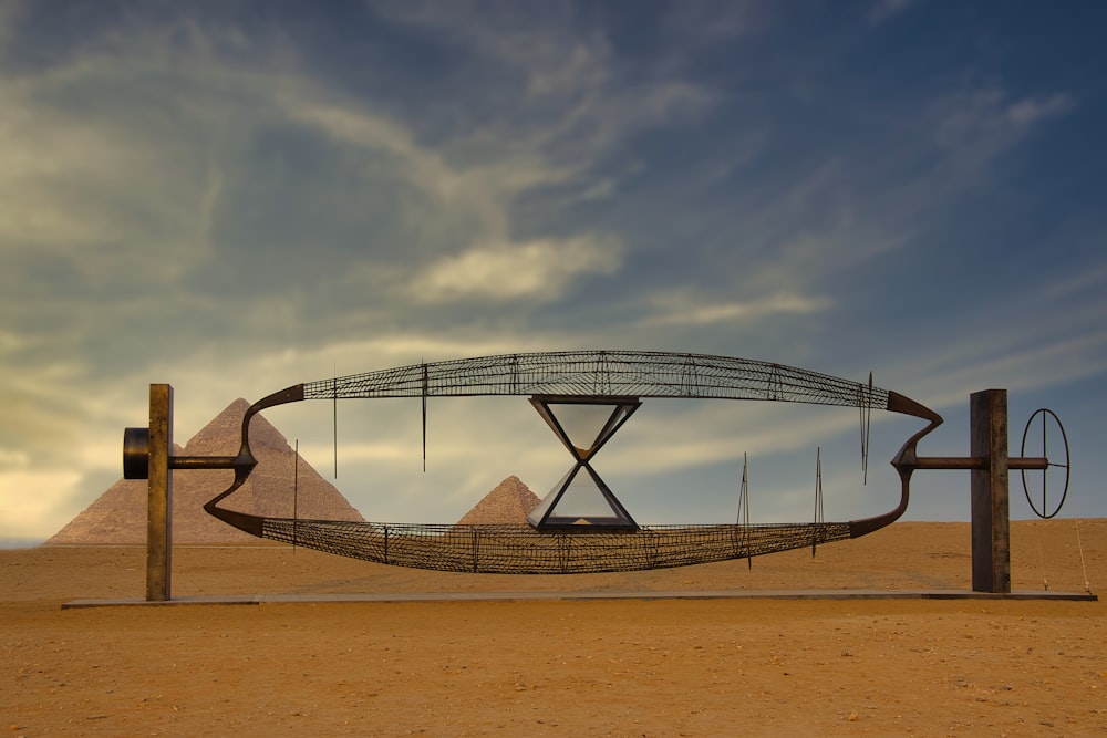 a sculpture in the middle of a desert with pyramids in the background