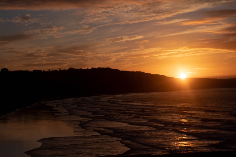 the sun is setting over the water at the beach