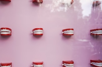 A pattern of red, wind-up toy chattering teeth is arranged against a light pink background, creating a whimsical and playful visual.