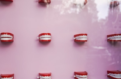 A pattern of red, wind-up toy chattering teeth is arranged against a light pink background, creating a whimsical and playful visual.