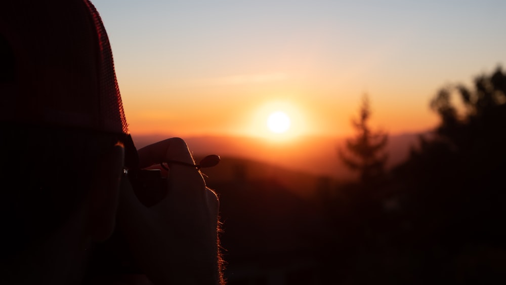 the sun is setting behind a person holding a cell phone
