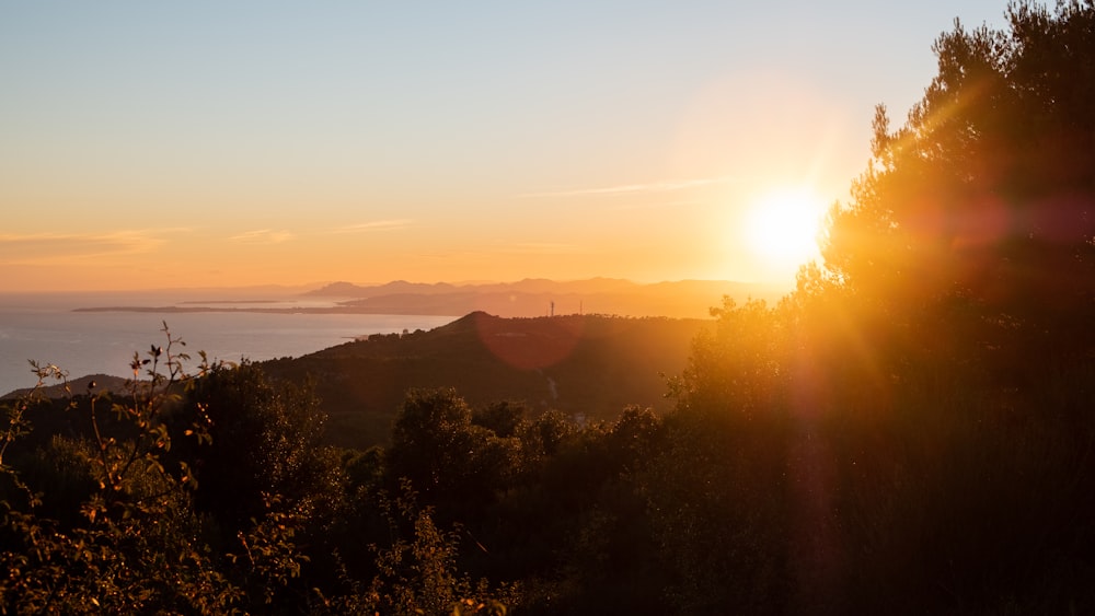 the sun is setting over the mountains and trees