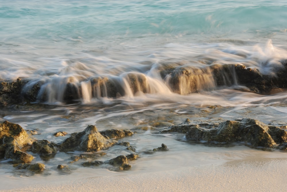 a close up of a wave on a beach with rocks