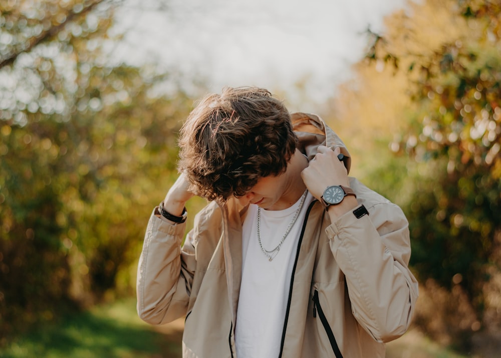 a man in a tan jacket is holding his hands to his ears