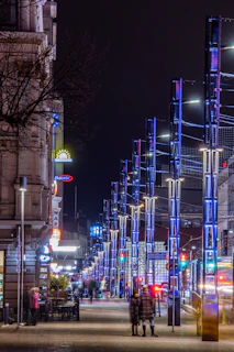 Scène urbaine animée avec des passants et des lumières de la ville la nuit.