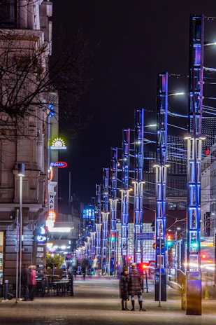 Scène urbaine animée avec des passants et des lumières de la ville la nuit.