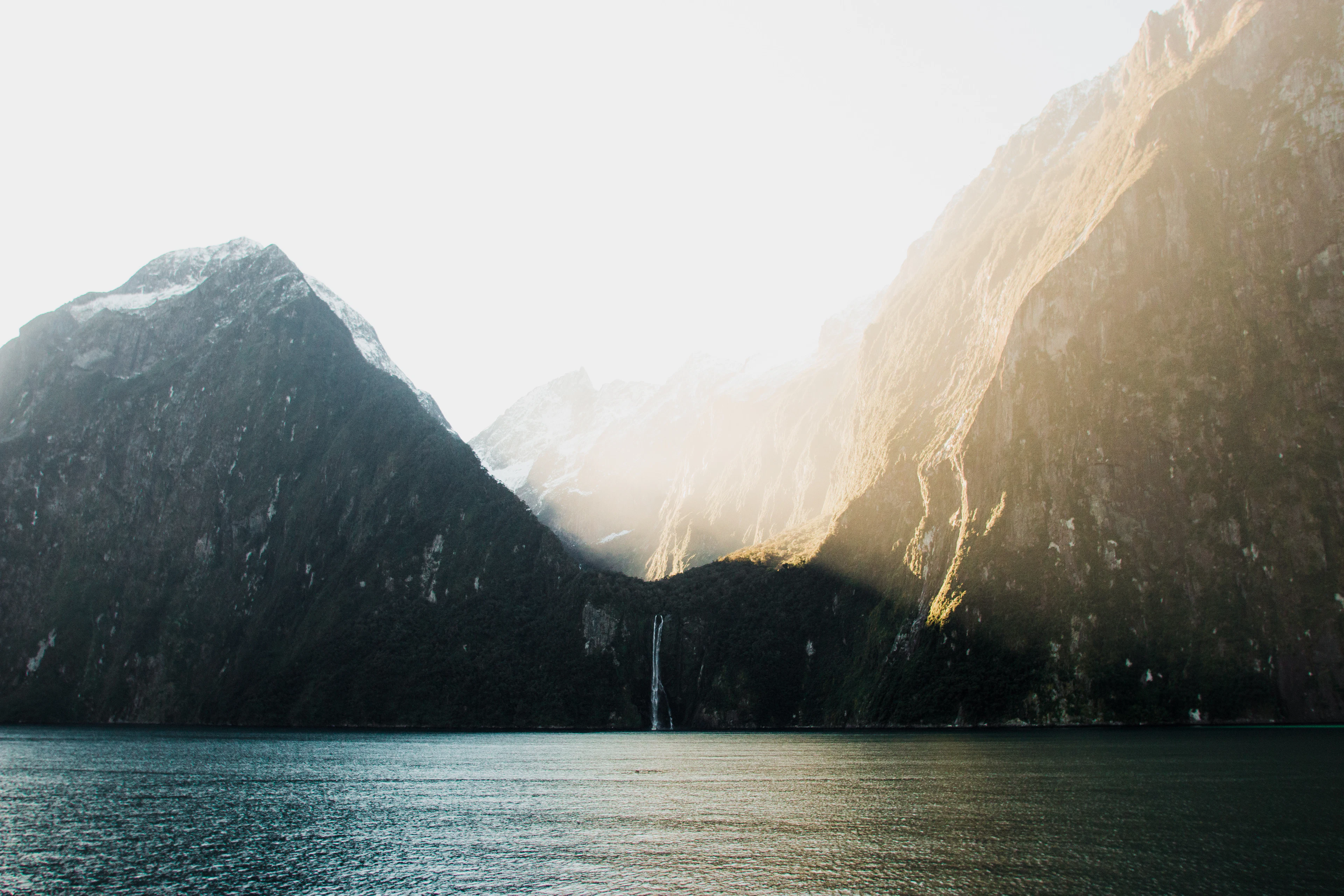 Sunlight falling on the steep walls of Milford Sound, with a waterfall and dark water below