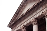 An architectural detail of a classical building featuring ornate Corinthian columns and a triangular pediment. The inscription 'FIDES ET PATRIA' is prominently displayed across the frieze.