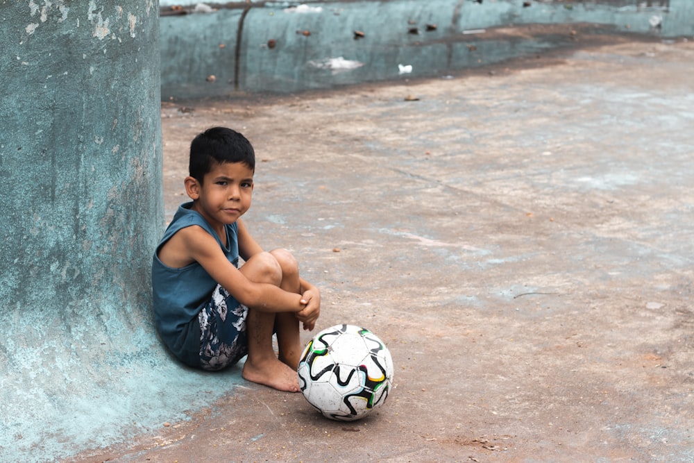 a young boy sitting on the ground with a soccer ball