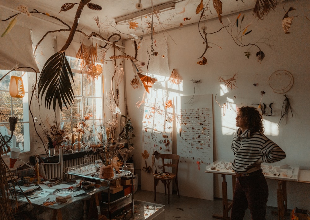 a woman standing in a room with a lot of plants hanging from the ceiling
