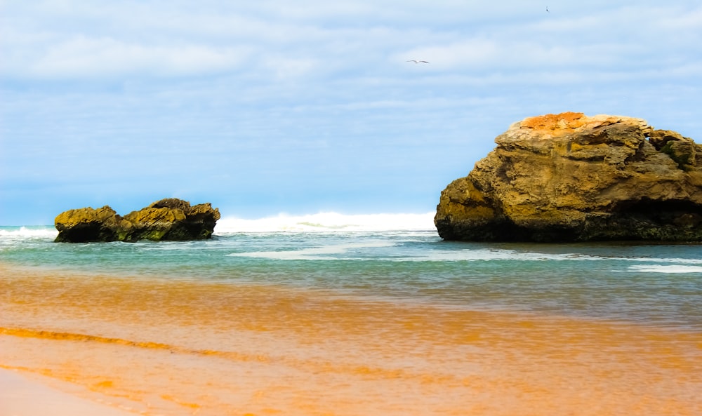 a rocky outcropping on the beach with waves coming in