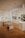 A spacious art gallery interior with wooden floors and several artworks displayed on the walls and pedestals. The ceiling is equipped with bright spotlights. There are two benches in the center for visitors to sit and observe the art pieces.