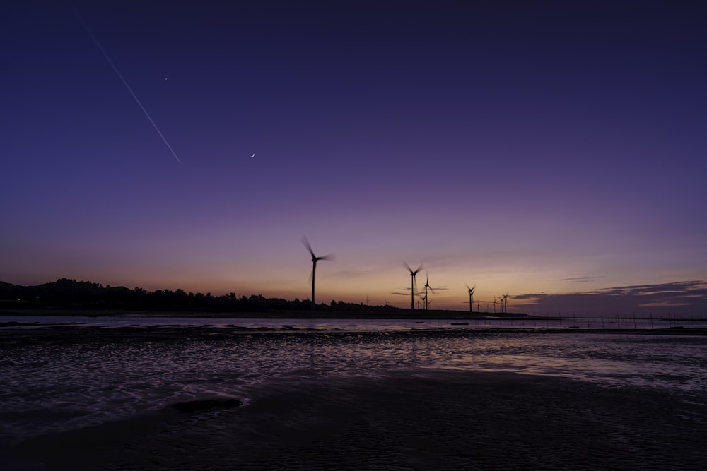 a group of windmills on a beach at sunset