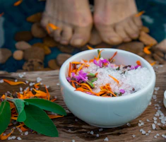 A serene foot soak setup with warm water, flower petals, and salts in a rustic ceramic bowl
