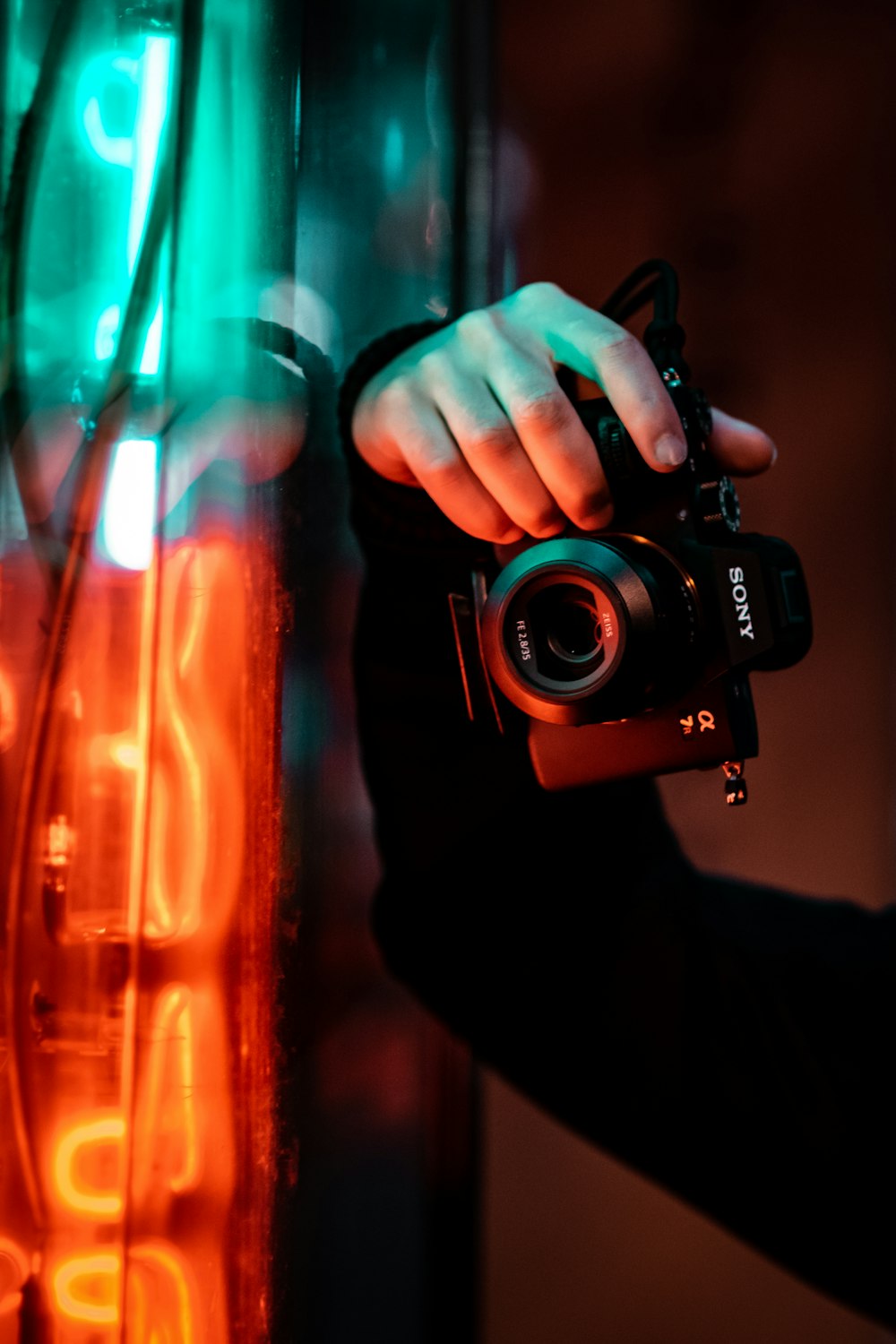a person holding a camera in front of a neon sign