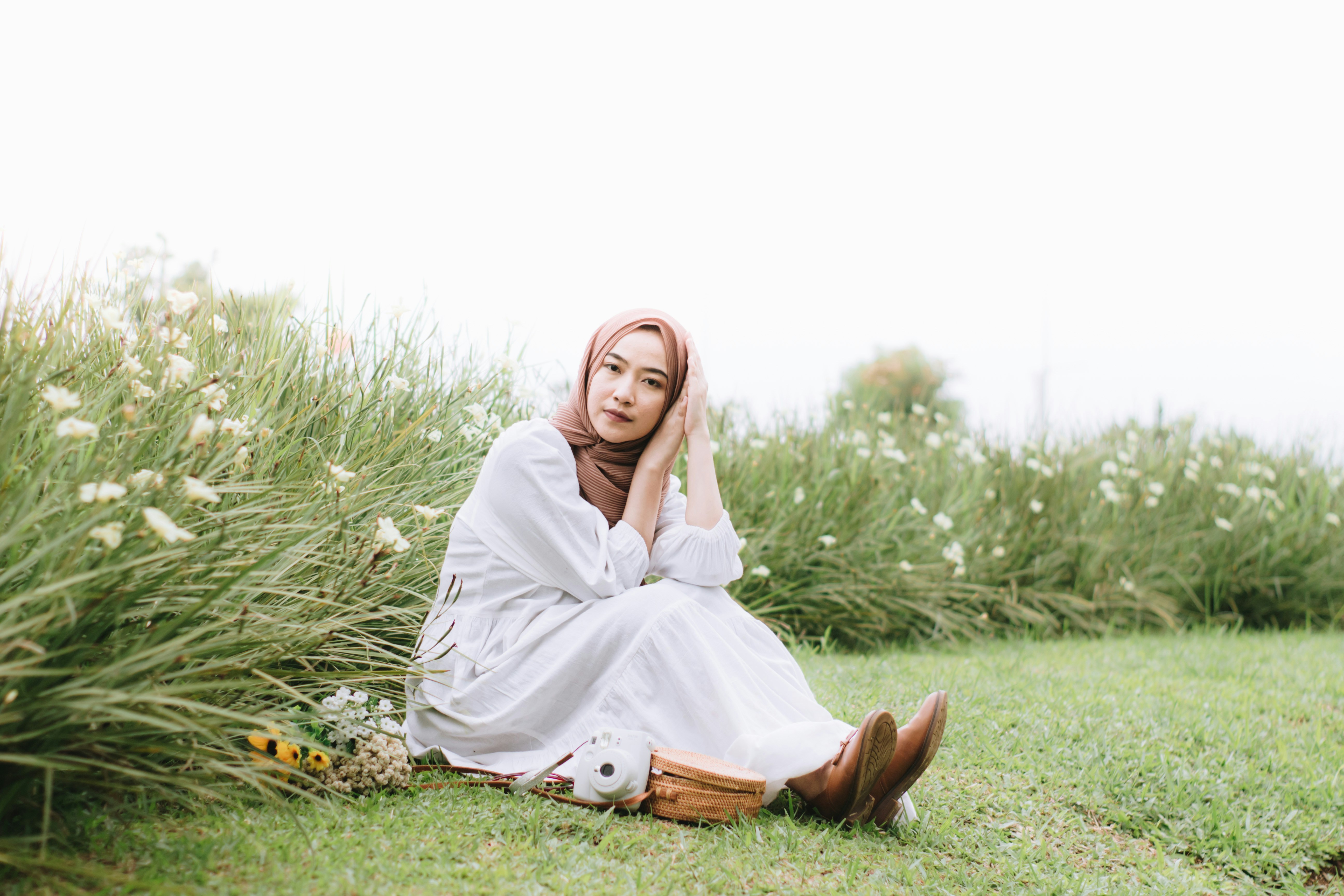 a woman in a white dress sitting in a field, 