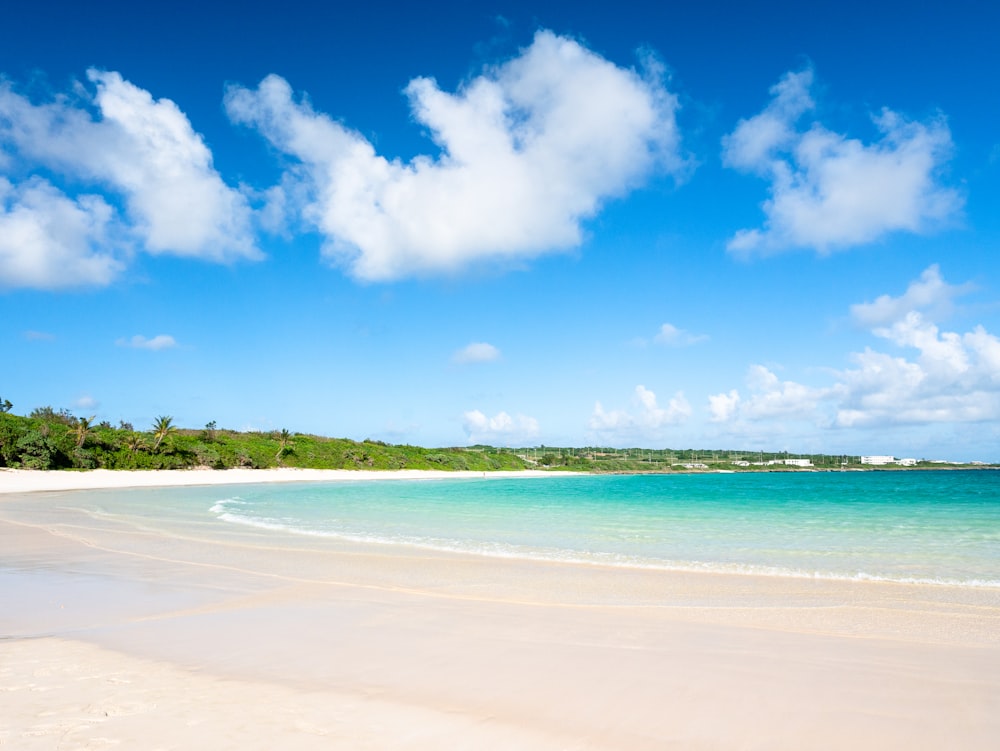 a sandy beach with clear blue water under a cloudy blue sky