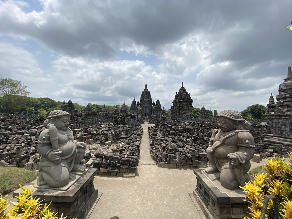 a stone walkway with statues of people and buildings in the background