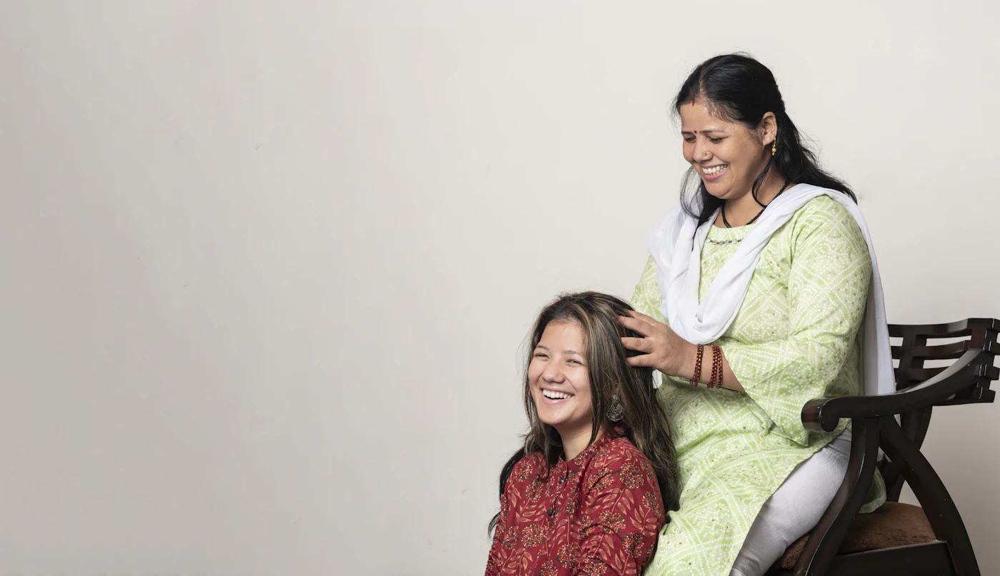 A mother and her teenage daughter laughing together as she braids her hair