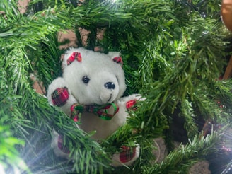 A cozy plush animal nestled among green leaves and soft candlelight.