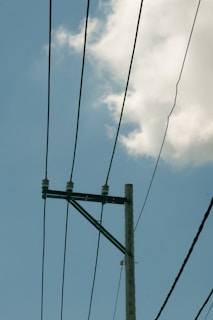 A utility pole stands against a backdrop of a partly cloudy sky. Several power lines extend horizontally from the pole, creating a pattern across the sky.
