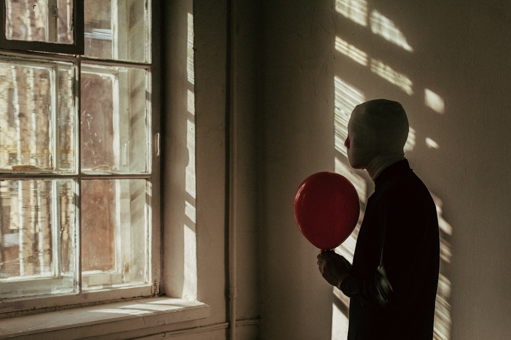 a man holding a red balloon in front of a window