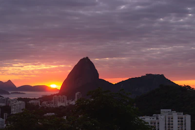 Sunset view over Rio de Janeiro with the silhouette of Sugarloaf Mountain and favela rooftops glowing warmly.