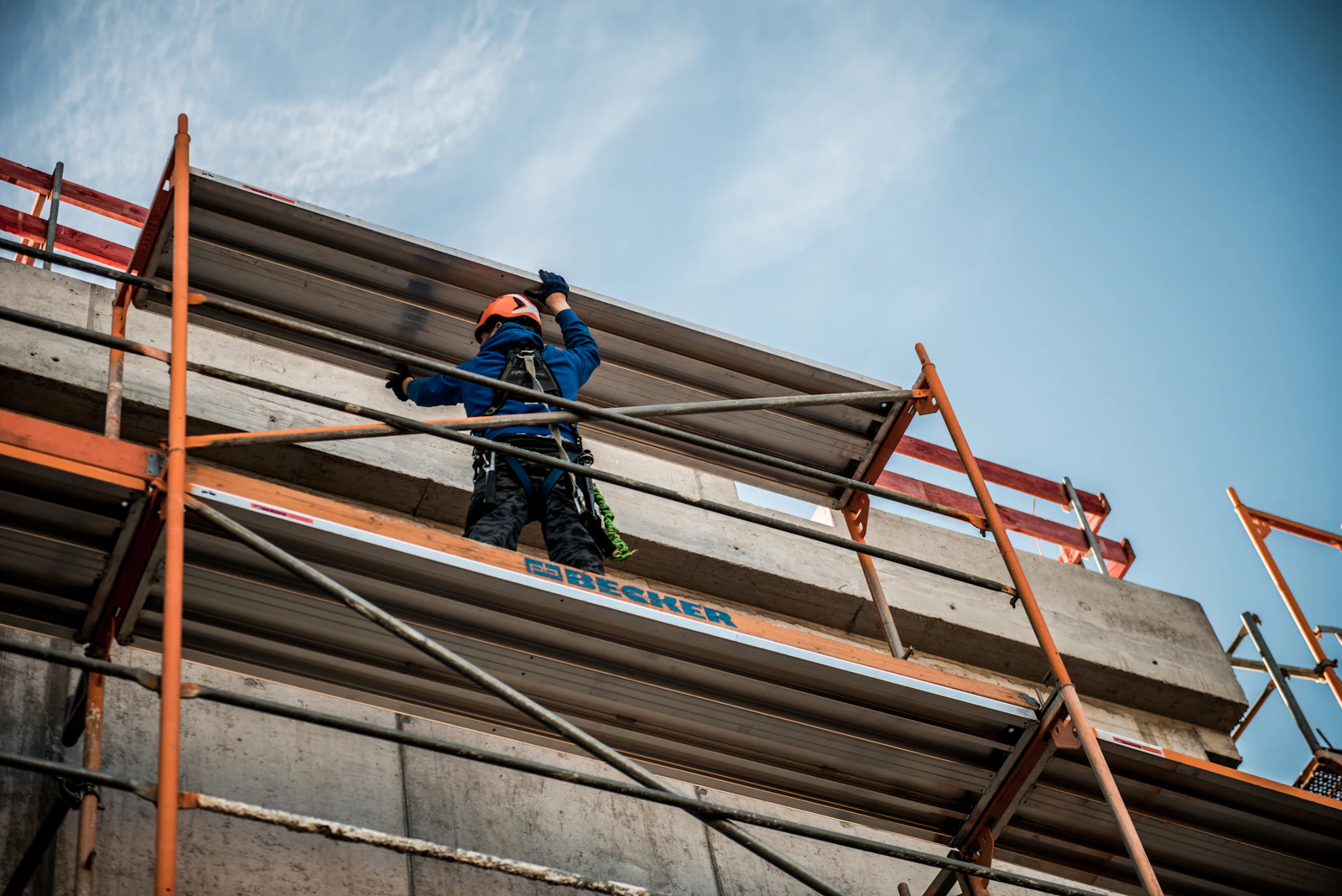 Gerüstbauer arbeitet auf einem Belag am oberen Rand einer Hausfassade