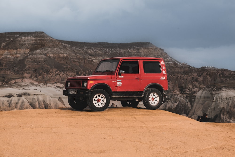 a red jeep parked on top of a sandy hill