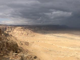 A cinematic shot of a desert landscape merging with Nordic fjords under a stormy sky.
