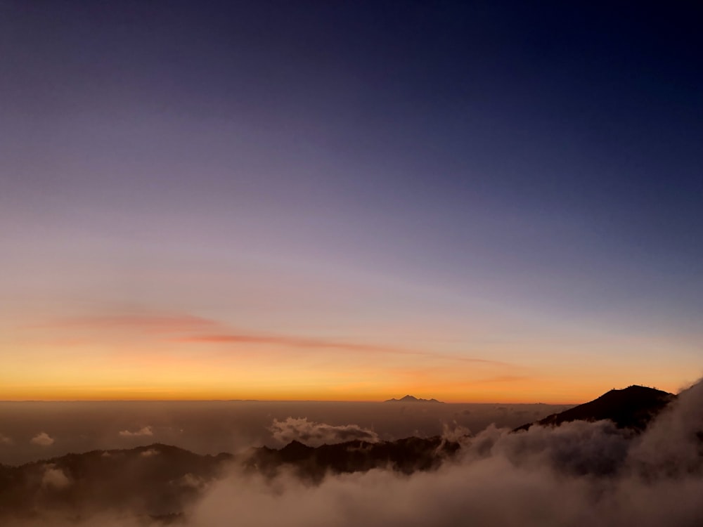 the sun is setting over a mountain with clouds