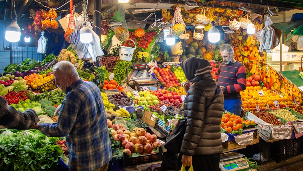 un groupe de personnes debout autour d’un stand de fruits et légumes