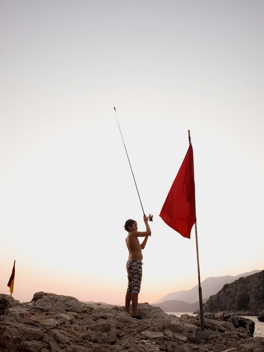 a man holding a red flag on top of a rocky beach