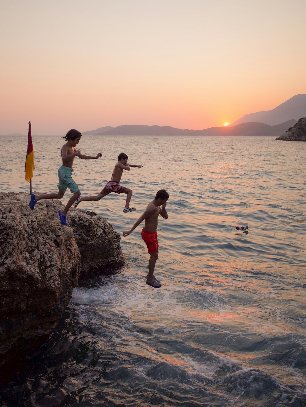 a group of kids jumping off rocks into the ocean