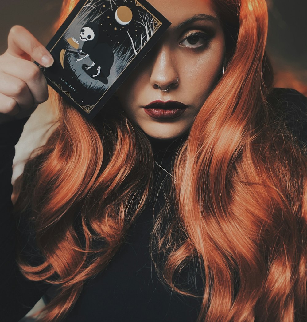 a woman with red hair holding up a card