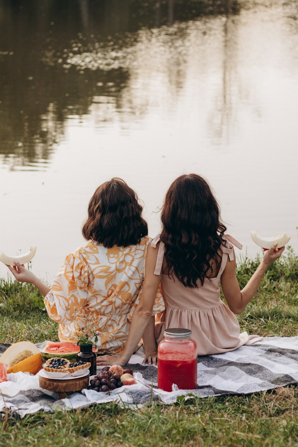 two women sitting on a blanket next to a body of water